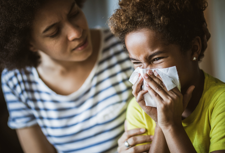 Ill girl blowing her nose at home while her mother is consoling her